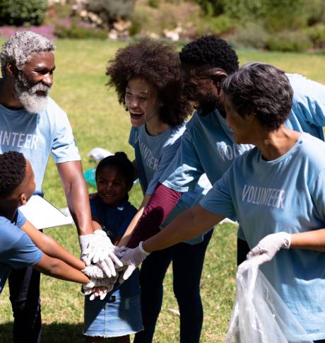 Multi-generation mixed race family enjoying their time at a garden, all wearing blue volunteer t shirts, collecting garbage, standing in a huddle, hand stacking, on a sunny day