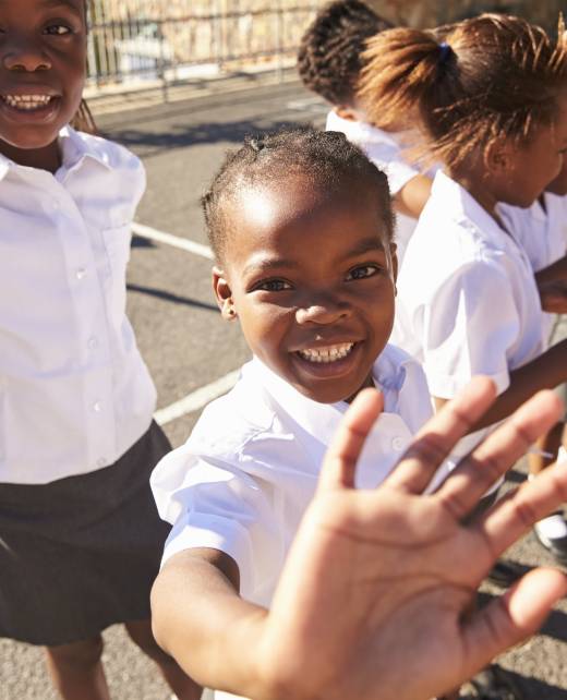 Young African schoolgirls in a playground waving to camera